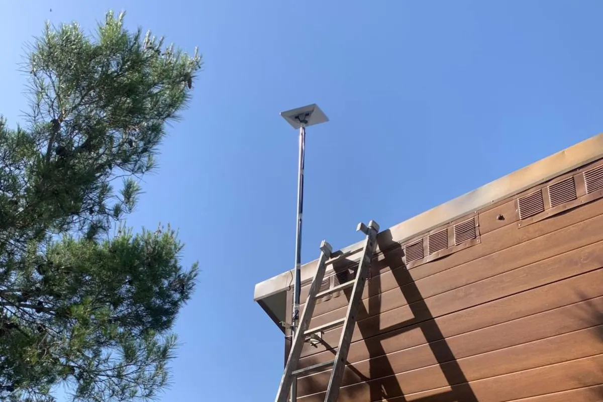 Antena de Starlink instalada por Red Huevo en un mástil por encima del tejado de una casa de madera, con un pino al lado y la escalera apoyada