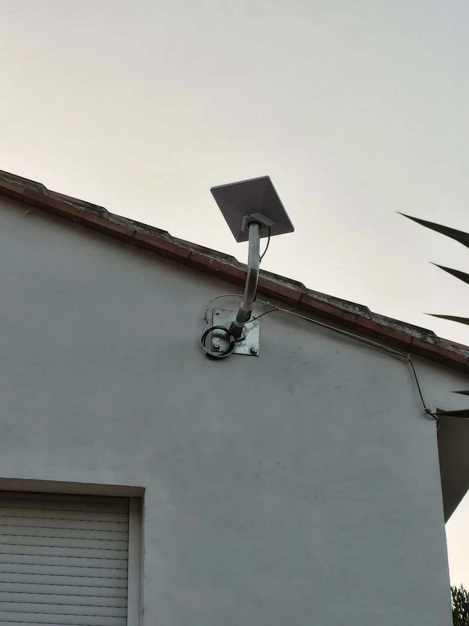 Antena Starlink Mini X instalada en una fachada de Ontinyent, sujeta con un tubo galvanizado curvado y una placa atornillada a la pared, junto al alero del tejado