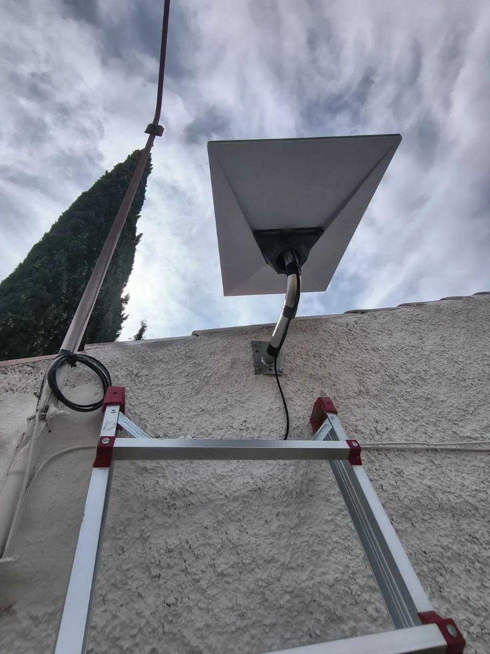 Parte trasera de la antena Starlink Standard 4 de Caudete vista desde abajo, con el tubo curvo galvanizado, la placa de fijación a la pared y el cable negro